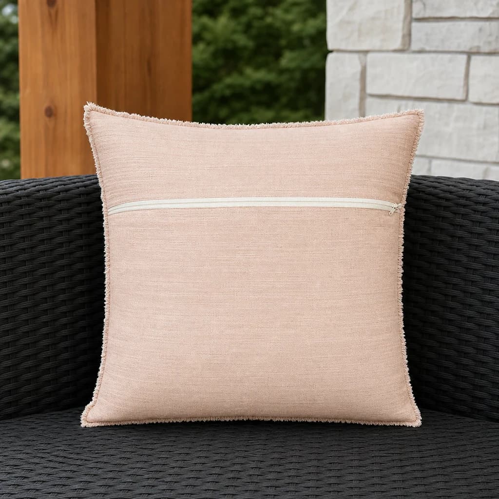 Ratana CU01314 Cova 14-inch blush toss pillow with zipper on a dark woven outdoor bench.