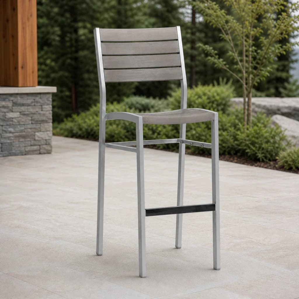 Ratana FN42941-B New Mirage armless stackable bar chair with gray slats, silver frame, and black footrest on a stone patio.